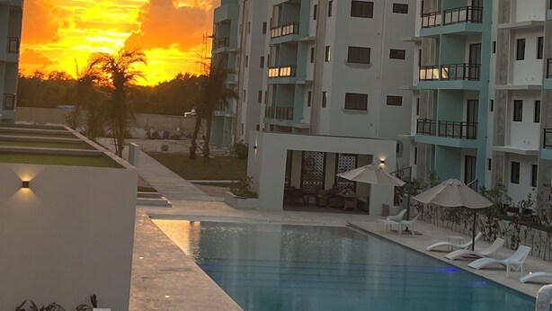 Ein modernes Hotel mit Schwimmbad, mehreren Balkonen und Blick auf den Sonnenuntergang.