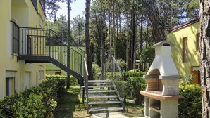 Ein Innenhof mit einer Treppe, die zu einem Balkon führt, umgeben von Bäumen und einem Grillplatz.