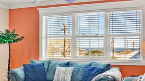 A teal sofa with multiple cushions, a palm tree with lights, and a view of the sea through large windows. - Beach Baby! Steps to South beach, Pool Access (Tybee Island)