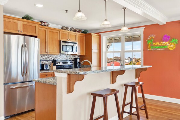 A modern kitchen with wooden cabinets, stainless steel appliances, a granite countertop, and a bar stool.