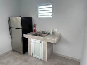 Una cocina compacta con refrigerador integrado, un lavamanos y un ventanal pequeño sobre el lavamanos.