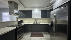 A modern kitchen with dark cabinets, a stainless steel refrigerator, and a white countertop. - Casa Paraíso - Your Tropical Escape in the heart of Loiza! (Loíza)