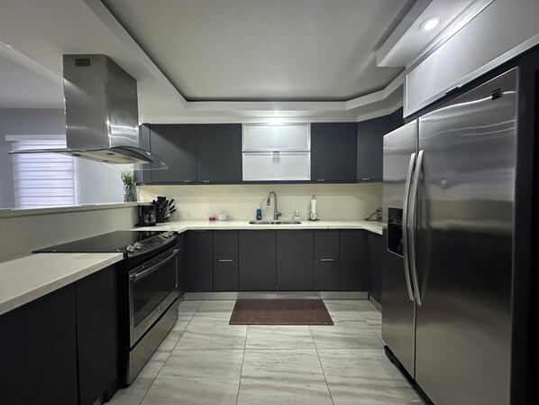 Una cocina moderna con armarios oscuros, un refrigerador de acero inoxidable y una encimera blanca.