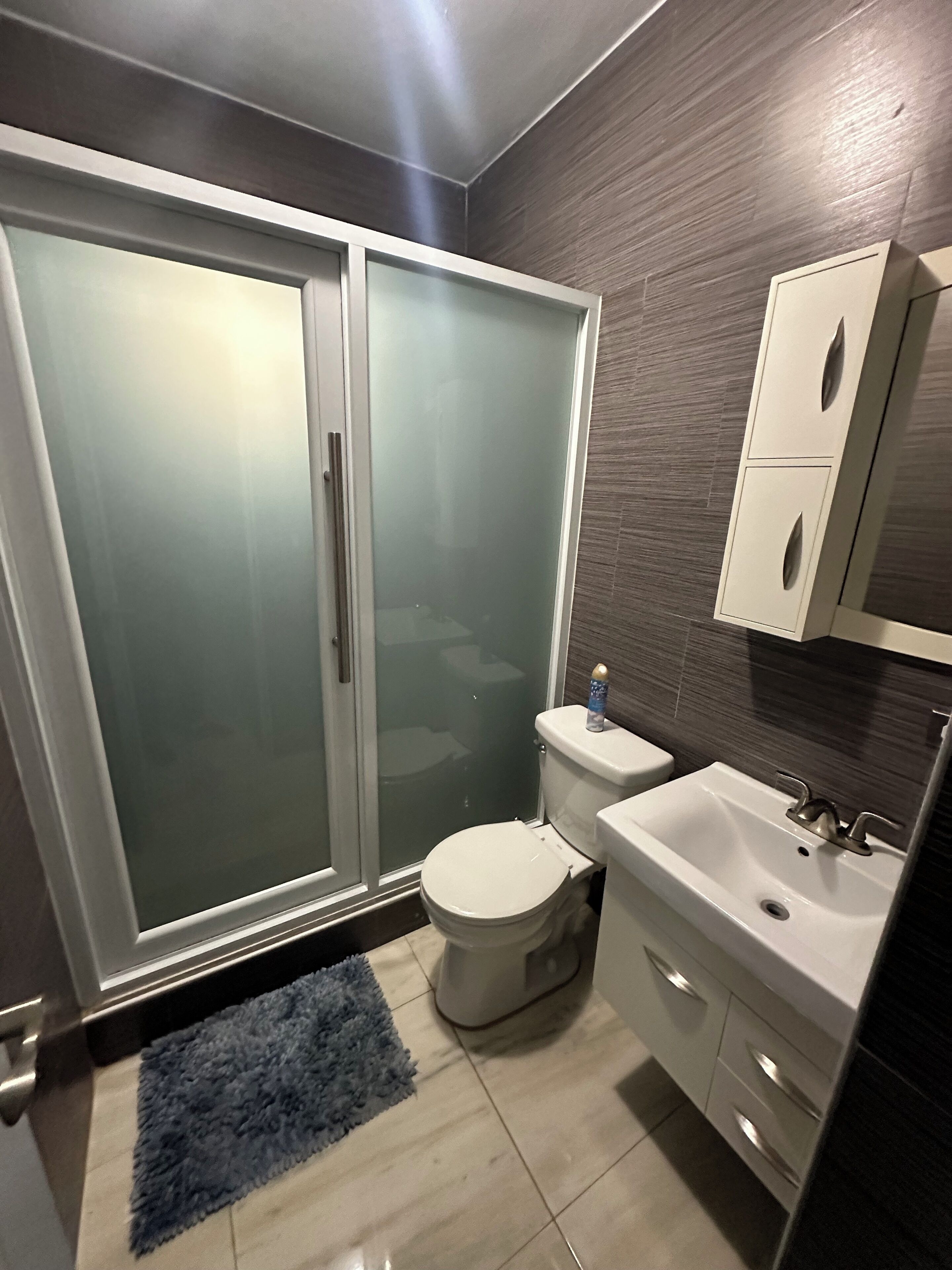 A modern bathroom with a glass-enclosed shower, a toilet, a sink, and a cabinet.