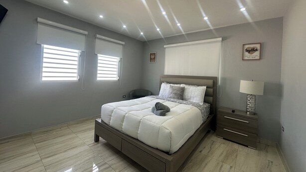 A bedroom with a bed, bedside tables, a chair, and a lamp. - Casa Paraíso - Your Tropical Escape in the heart of Loiza! (Loíza)