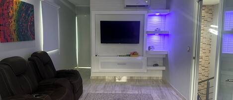Una sala de estar moderna con televisor de pantalla plana, sofás de cuero, alfombra estampada y mueble de entretenimiento empotrado con iluminación ambiental.