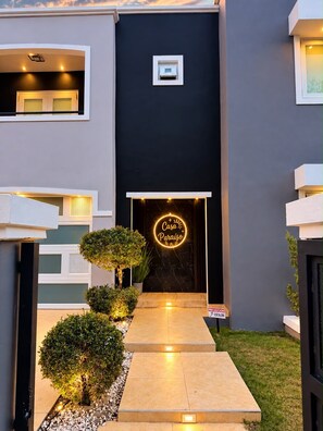 A modern building entrance with a neon sign, a small window, and a pathway leading to the door.
