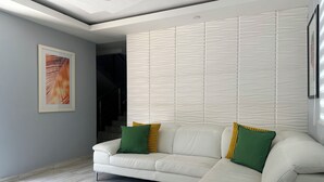 A modern living room with a white sectional sofa, a framed abstract painting, and a textured wall panel. - Casa Paraíso - Your Tropical Escape in the heart of Loiza! (Loíza)