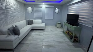 A modern living room with a sectional sofa, a TV on a green cabinet, and decorative wall panels. - Casa Paraíso - Your Tropical Escape in the heart of Loiza! (Loíza)