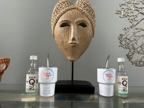 Una mesa con una escultura de máscara de madera, dos botellas de Don Q Coco y una botella de vidrio.
