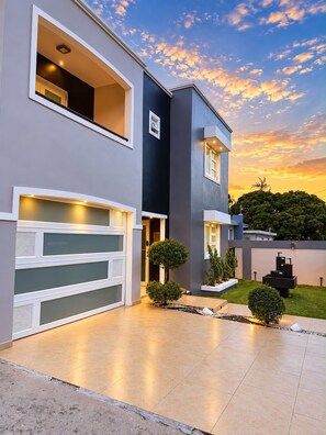 A modern two-story house with a garage, a well-maintained lawn, and a sunset sky.