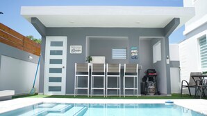 A modern outdoor patio with a pool, a barbecue grill, and a covered seating area. - Casa Paraíso - Your Tropical Escape in the heart of Loiza! (Loíza)
