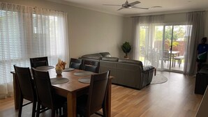A modern living room with a dining area, a sofa, and a ceiling fan. - Modern Four Bedroom Holiday Home Available in Deebing Heights (Deebing Heights)