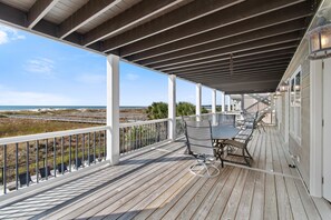 Una terraza de madera con una mesa y sillas, con vista a una playa y dunas.