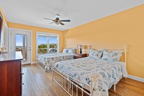 Un dormitorio con dos camas, un ventilador de techo, un aparador de madera y vistas al exterior.