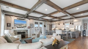 Amplia sala de estar con chimenea, televisor grande y comedor con cocina al fondo.