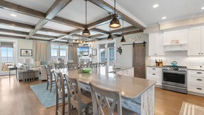 Una cocina amplia con una isla grande, vigas de madera, armarios blancos y electrodomésticos modernos.