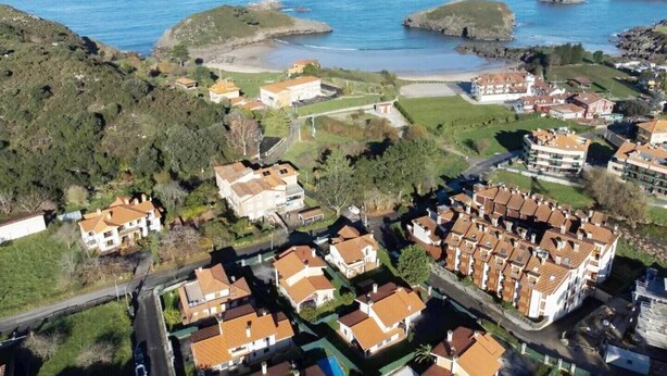 Vista aérea de una zona residencial costera con casas, una playa y afloramientos rocosos.