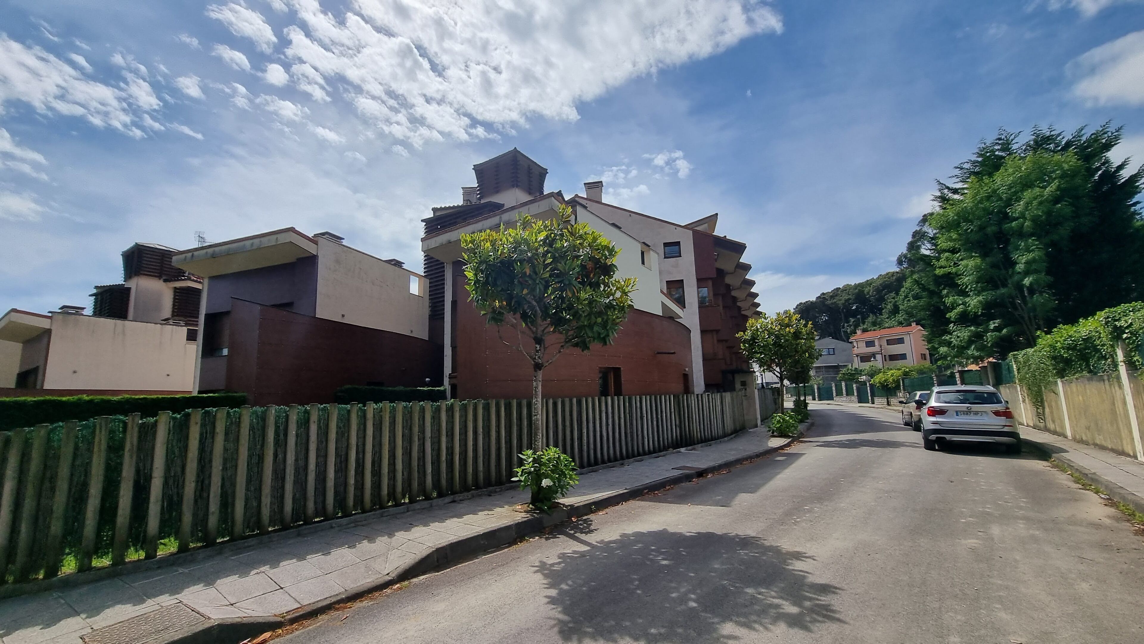 Una calle residencial con casas modernas, una valla de madera y un coche estacionado.