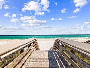 A wooden boardwalk leading to a beach with a clear view of the ocean.
