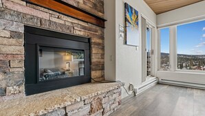A stone fireplace with a black surround, a view of a snowy landscape through large windows, and a painting on the wall. - Ski-in/Ski-out, Covered Parking, Hot Tub! (Durango)
