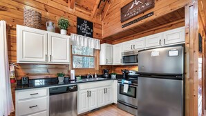 Een keuken in chaletstijl met witte kasten, roestvrijstalen apparatuur en een houten plafond.