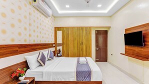 Ein modernes Hotelzimmer mit großem Bett, Holz-Kopfteil, einem Flachbildfernseher an der Wand und einem Deckenventilator.