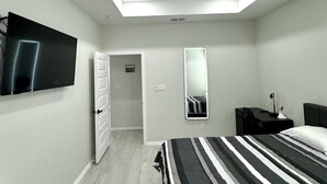 Una camera da letto moderna con un letto, una televisione a schermo piatto, una ventola a soffitto e una porta che dà su un'altra stanza.