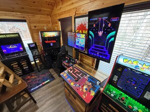 Quarto com vários jogos de fliperama, incluindo Pac-Man e Donkey Kong, e uma tela grande exibindo um jogo.
