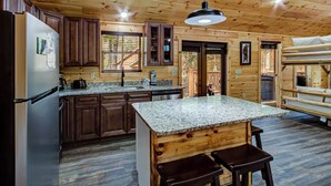 A cabin-style kitchen with wooden walls, a granite countertop island, and a built-in bench. - Newly Built-Sleeps 8 w/Fire Pit, Arcade lineup, Hot Tub, Horseshoe Pit & BBall (Sevierville)