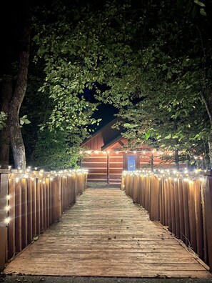 A wooden pathway leading to a building with string lights. - Newly Built-Sleeps 8 w/Fire Pit, Arcade lineup, Hot Tub, Horseshoe Pit & BBall (Sevierville)