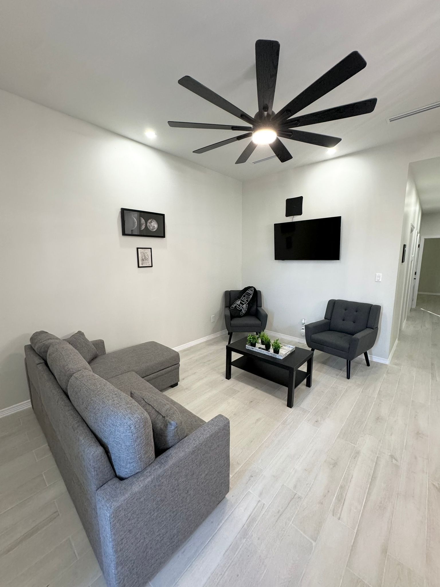 A modern living room with a sectional sofa, two armchairs, a coffee table, and a ceiling fan.