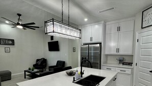 Una cocina moderna con una isla grande, muebles blancos, un refrigerador de acero inoxidable y una araña.
