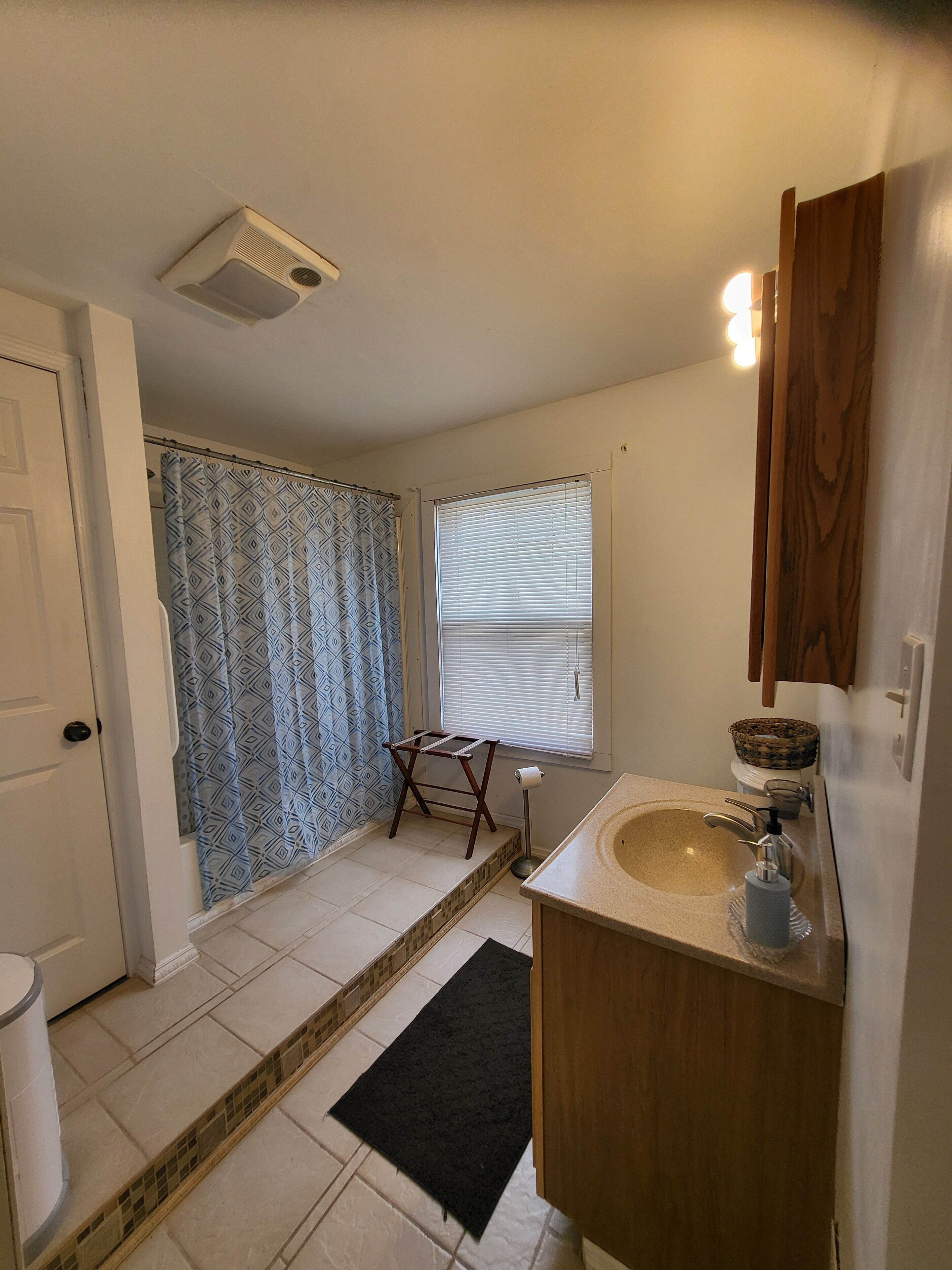 A bathroom with a sink, toilet, shower, and a small wooden stool.