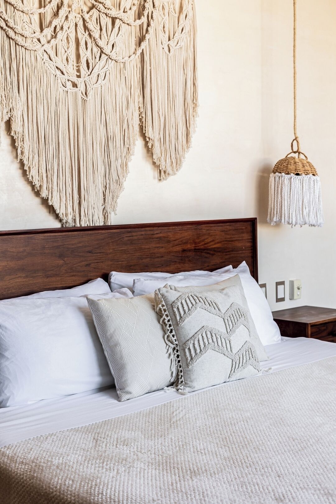 A bed with white linens, a macrame wall hanging, and a macrame pendant light.