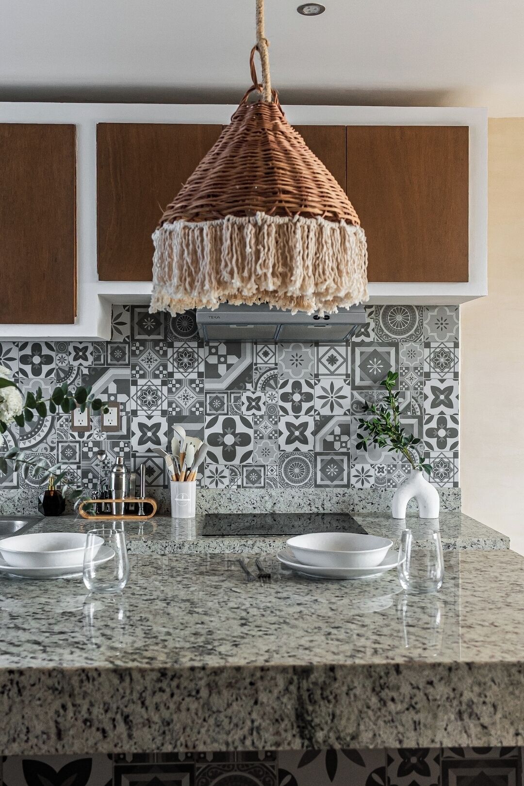 A kitchen with a hanging wicker light fixture, a patterned backsplash, and a granite countertop.