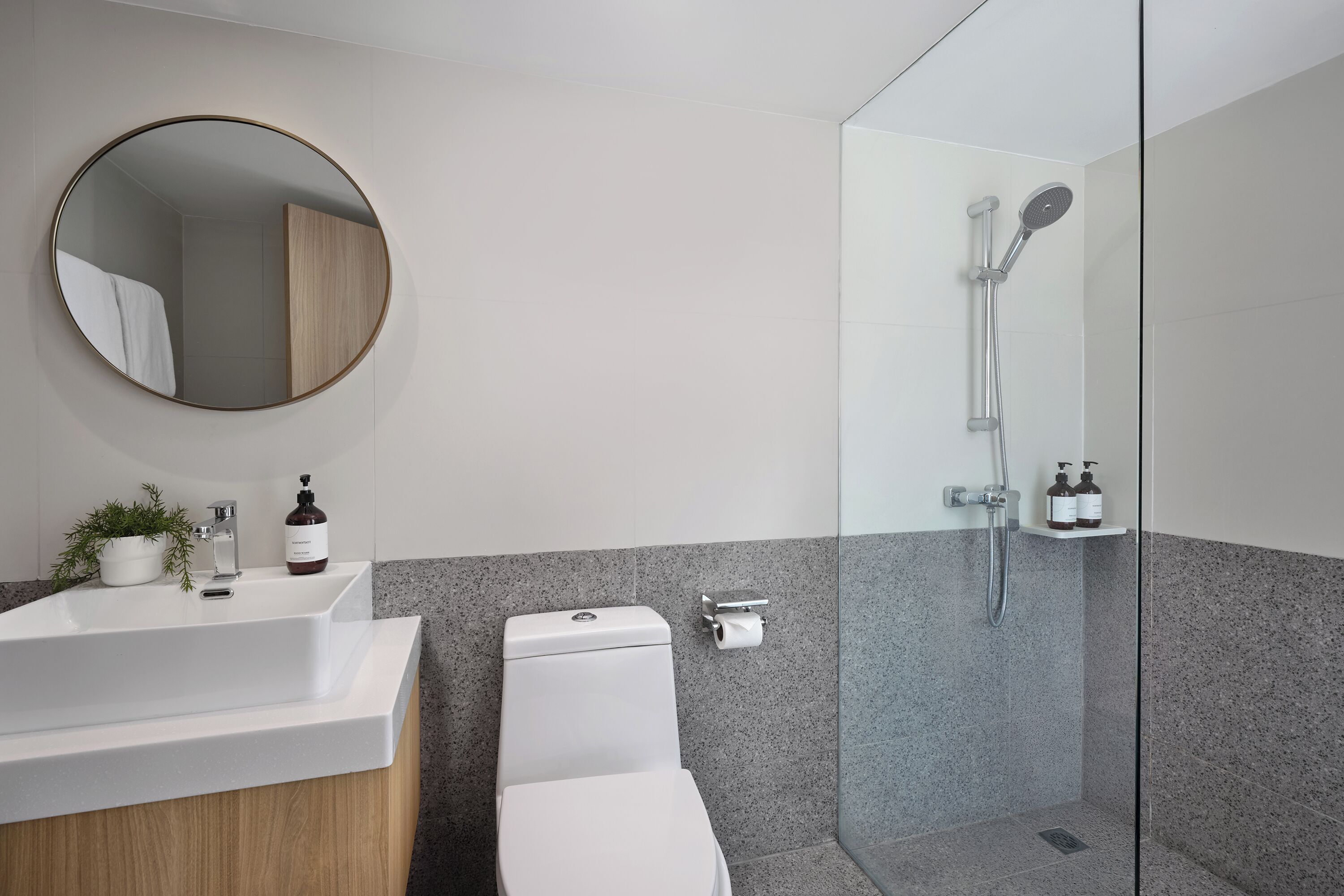 A modern bathroom with a round mirror, white sink, and glass-enclosed shower.
