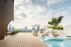 Un espace piscine aménagé sur le toit, avec des chaises longues, des parasols et une vue panoramique sur la ville.