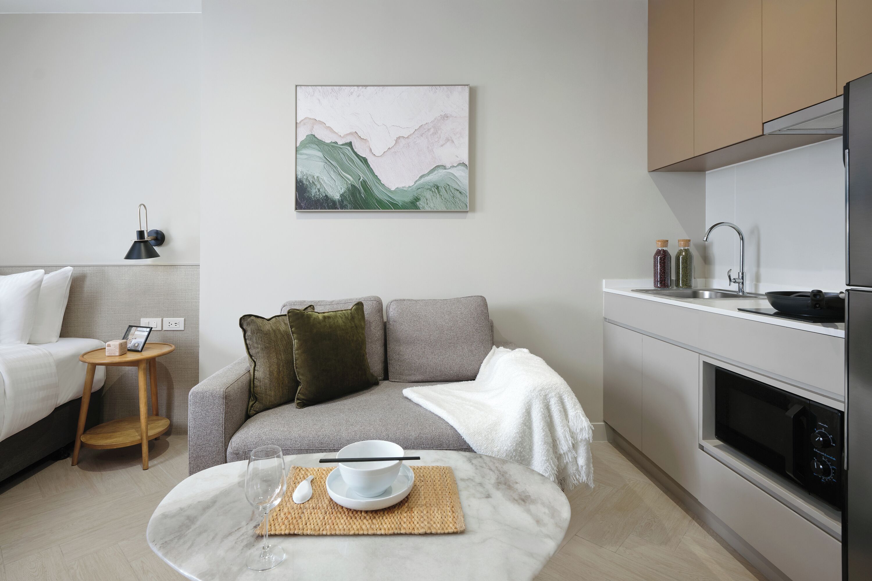 A modern living room with a sofa, a coffee table, and a kitchen area with a microwave and sink.
