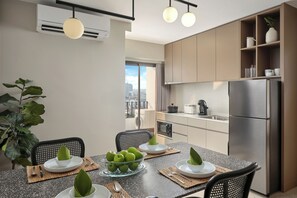 A modern kitchen with a stainless steel refrigerator, a dining table set with green leaves, and a large window offering a city view.