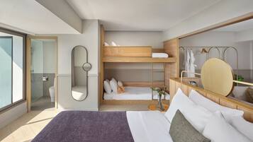 Una habitación de hotel moderna con una cama grande, una cama litera, un baño con puerta de cristal y un espejo grande.