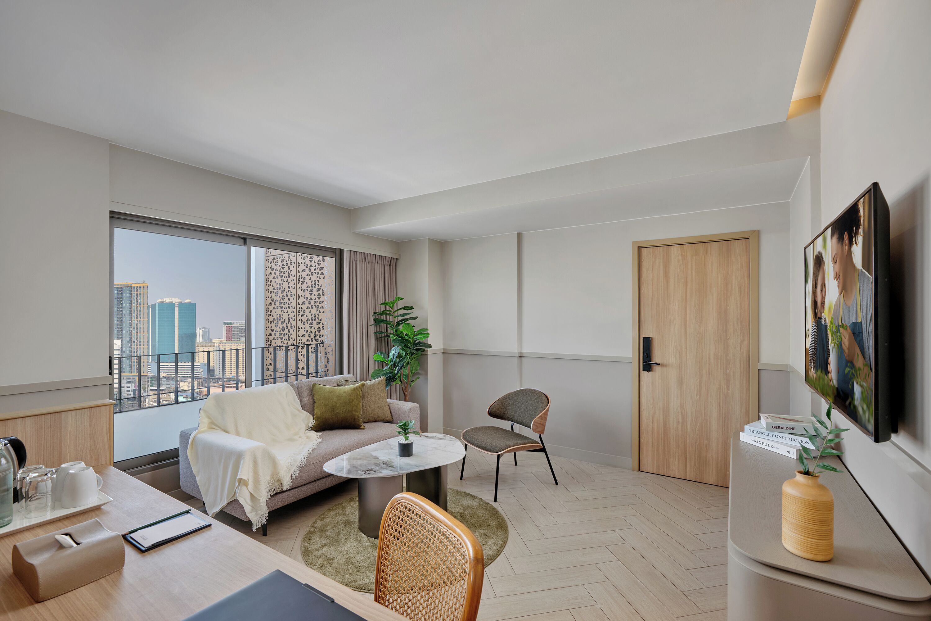 A modern living room with a sofa, coffee table, and chairs, a dining area with a table and chairs, a large window with a city view, and a door.