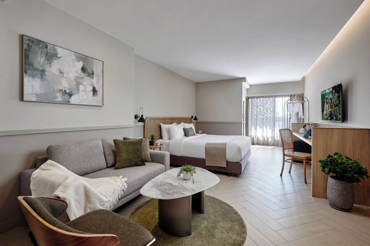 Una habitación de hotel moderna con sofá, cama, escritorio y un cuadro abstracto grande.