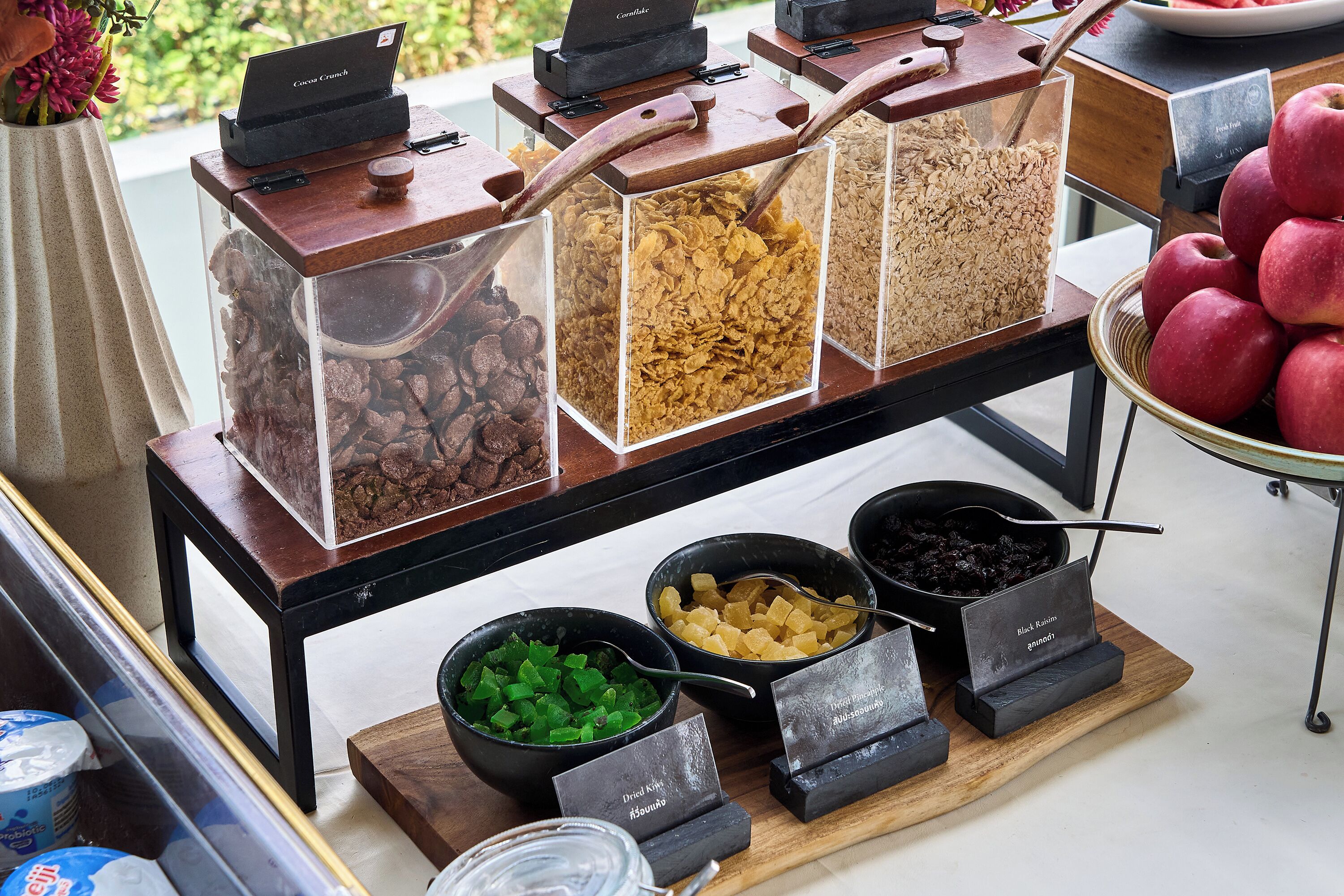 Un buffet avec différents plats présentés dans des récipients et des bols, un ordinateur portable posé sur un support et un saladier rempli de pommes.
