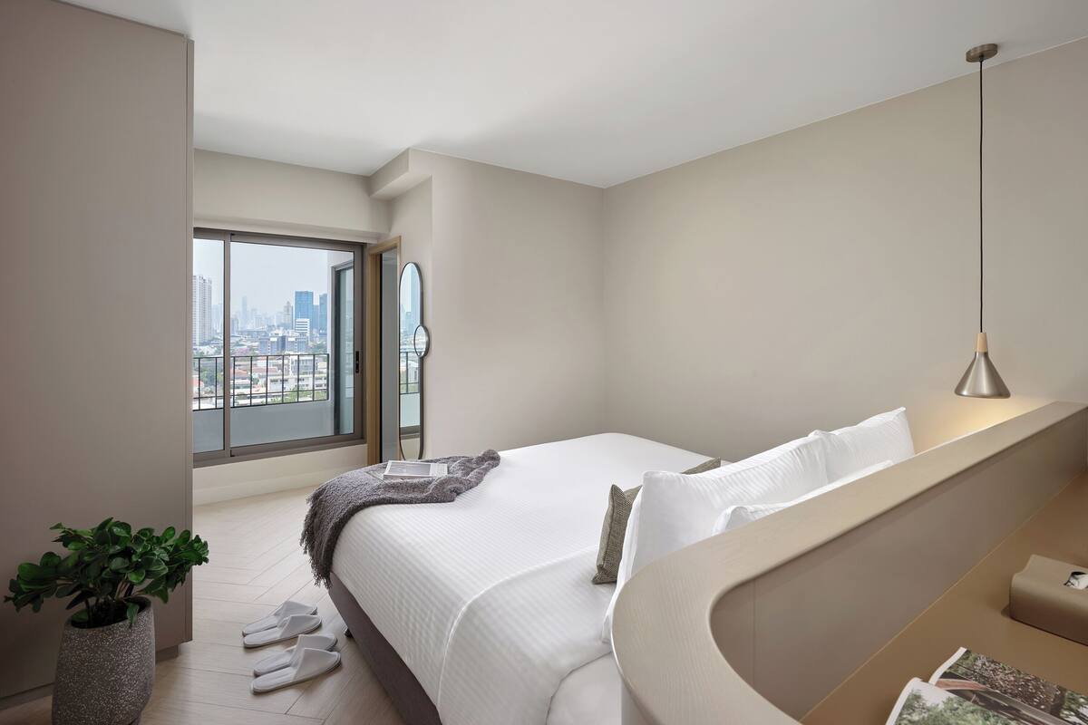 Un dormitorio moderno con una cama grande, vistas a la ciudad y una planta en maceta.