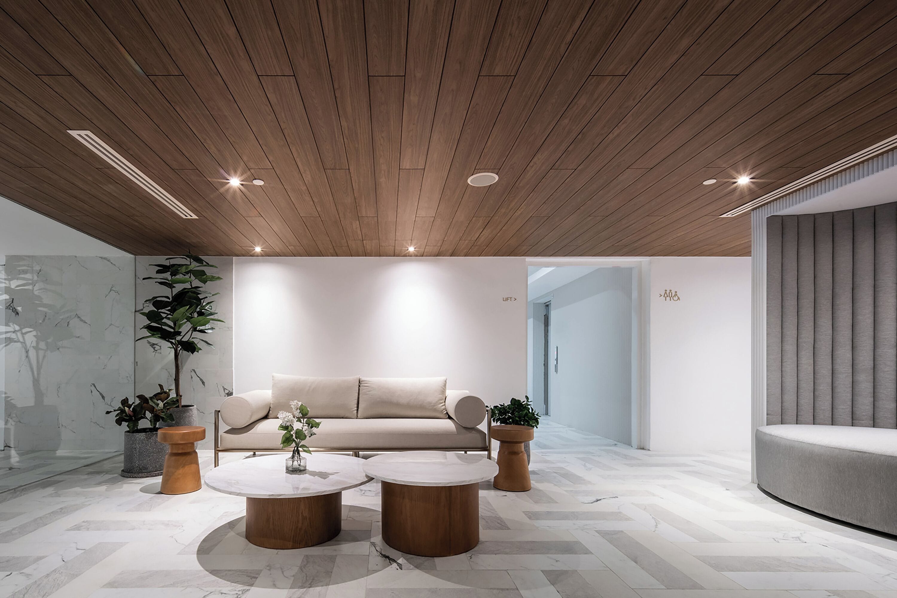 A modern interior with a wooden ceiling, a beige sofa, and two round wooden tables.