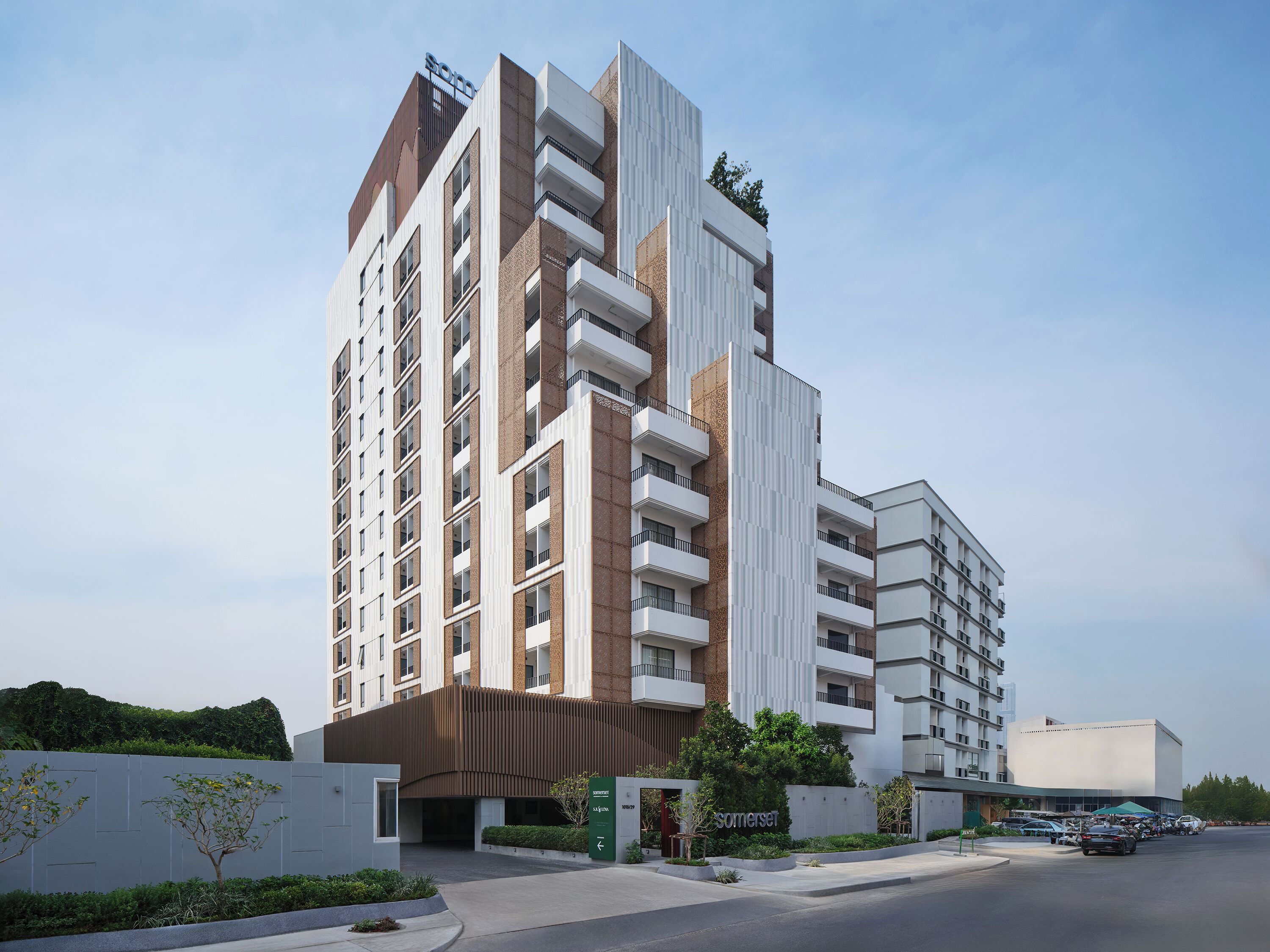A modern high-rise hotel with multiple balconies, a prominent entrance, and a parking area.