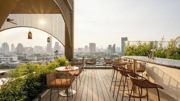 Un bar sul tetto con sedie e tavoli in vimini, affacciato su un panorama urbano.