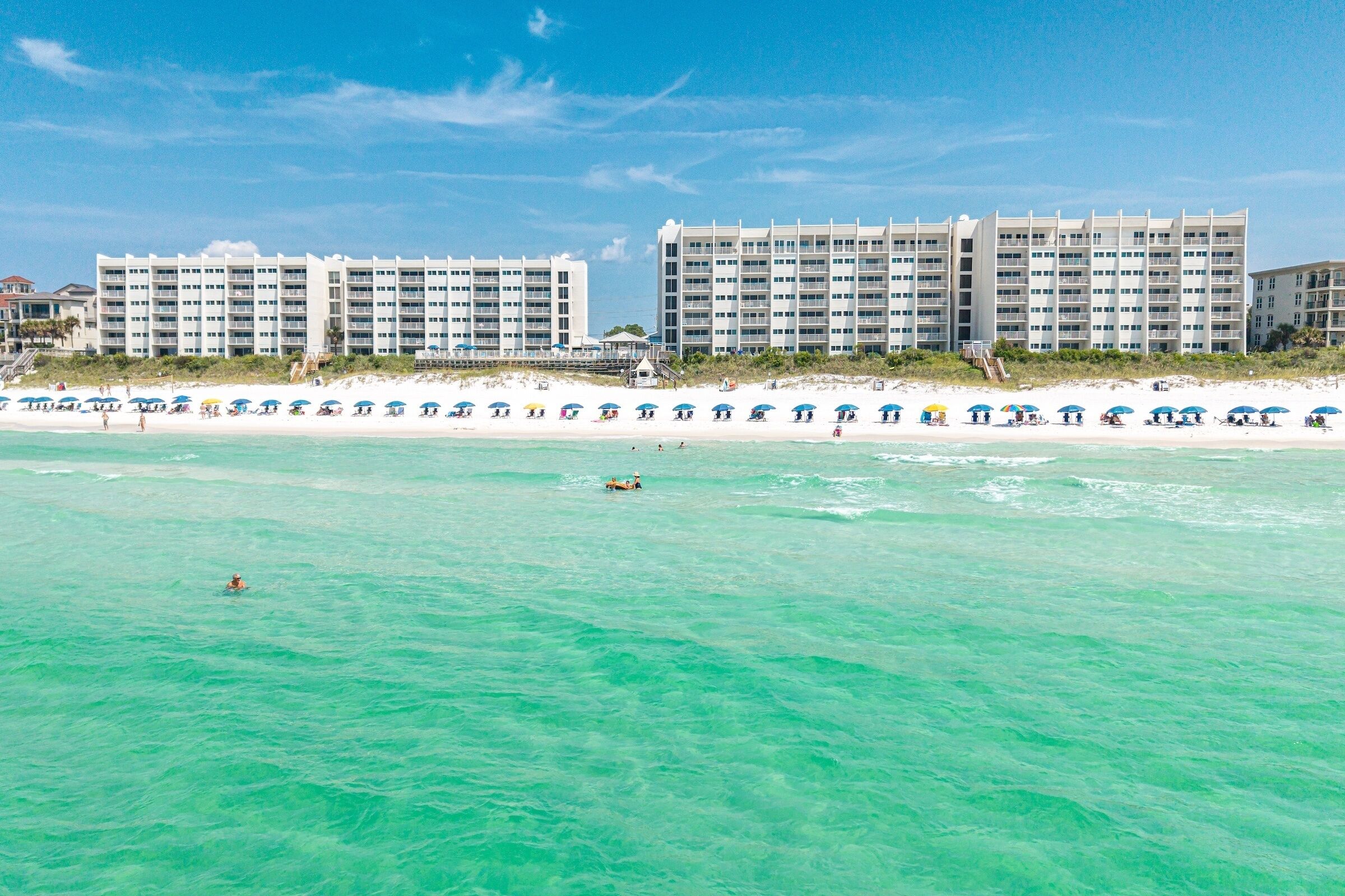 Un hotel fronte spiaggia con numerosi balconi, una spiaggia sabbiosa e acque cristalline color turchese.