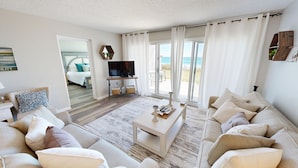 Un salón espacioso con un sofá grande, una mesa de centro y un televisor. Cuenta con un balcón con vistas al mar.